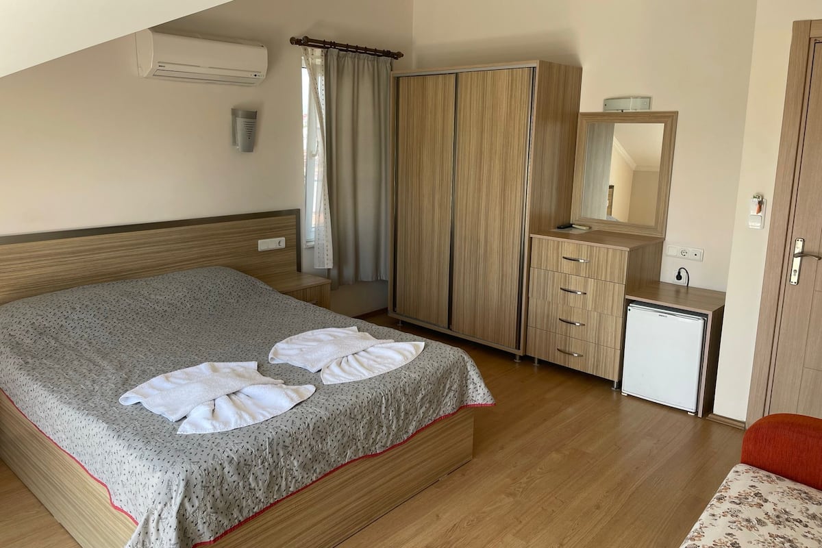 Habitación de hotel con cama, armario, escritorio pequeño con espejo y unidad de aire acondicionado.