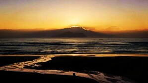 A beach with a sunset, waves, and a silhouette of a mountain in the distance. - Qi Hua Zhen Ju Homestay (Toucheng)