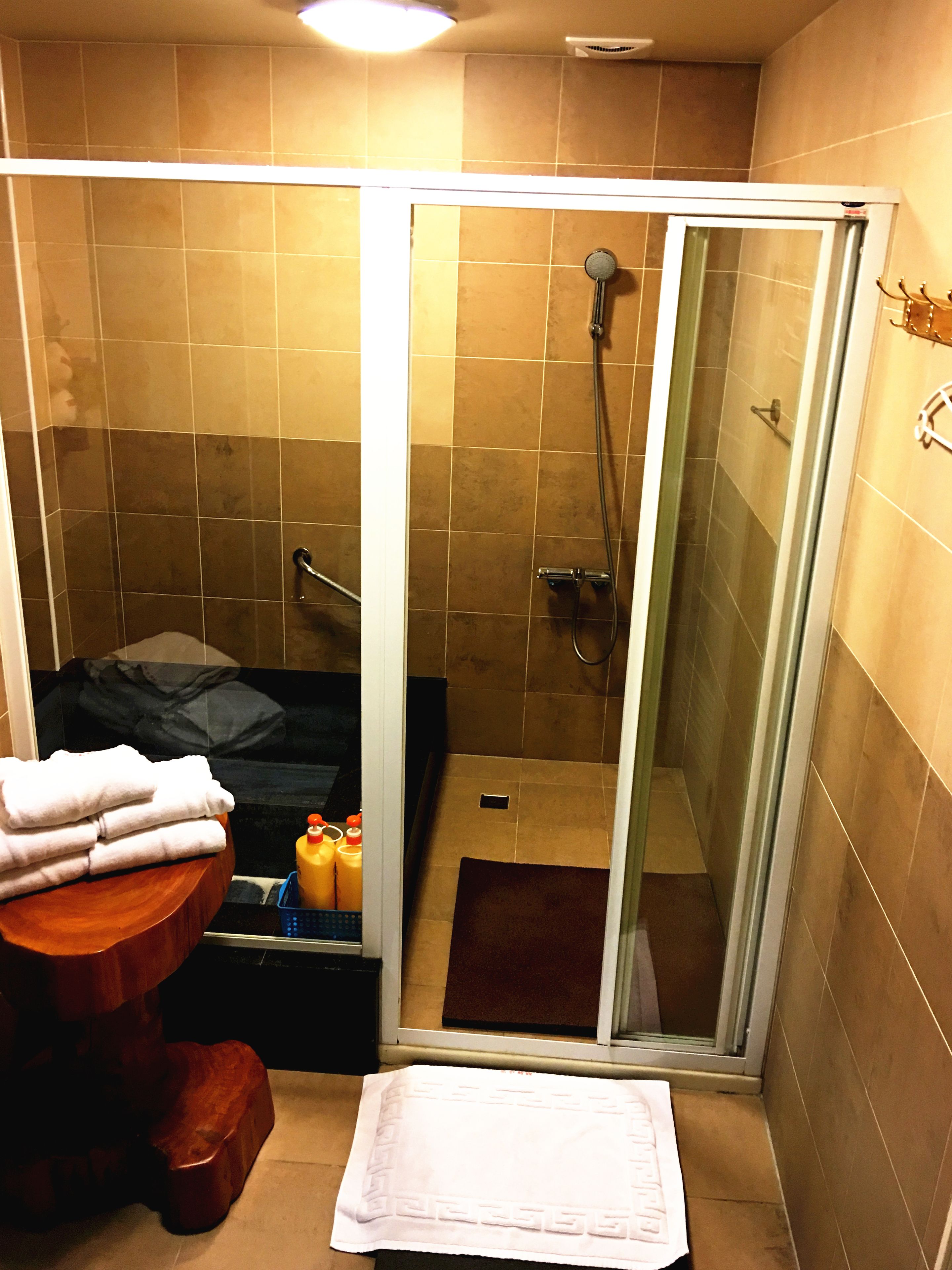 Une salle de bain avec une douche, un lavabo avec une pile de serviettes et des articles de toilette posés sur le comptoir.