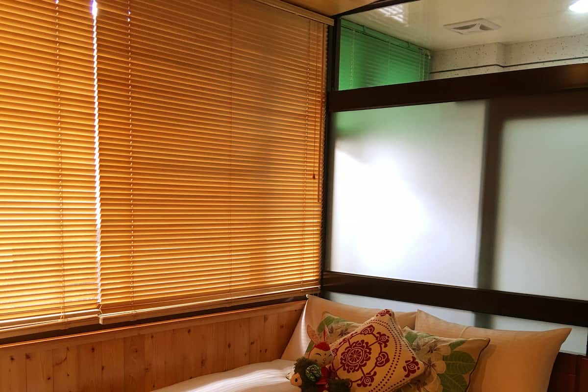 Un lit avec une couvre-lit à motifs, deux oreillers et une fenêtre avec des stores.
