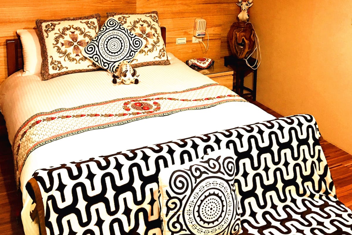 Une chambre à coucher avec une tête de lit en bois, un lit recouvert d’une literie à motifs, un vélo fixé au mur et un élément décoratif mural.