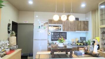 A modern kitchen with a wooden dining table, hanging pendant lights, and a refrigerator.