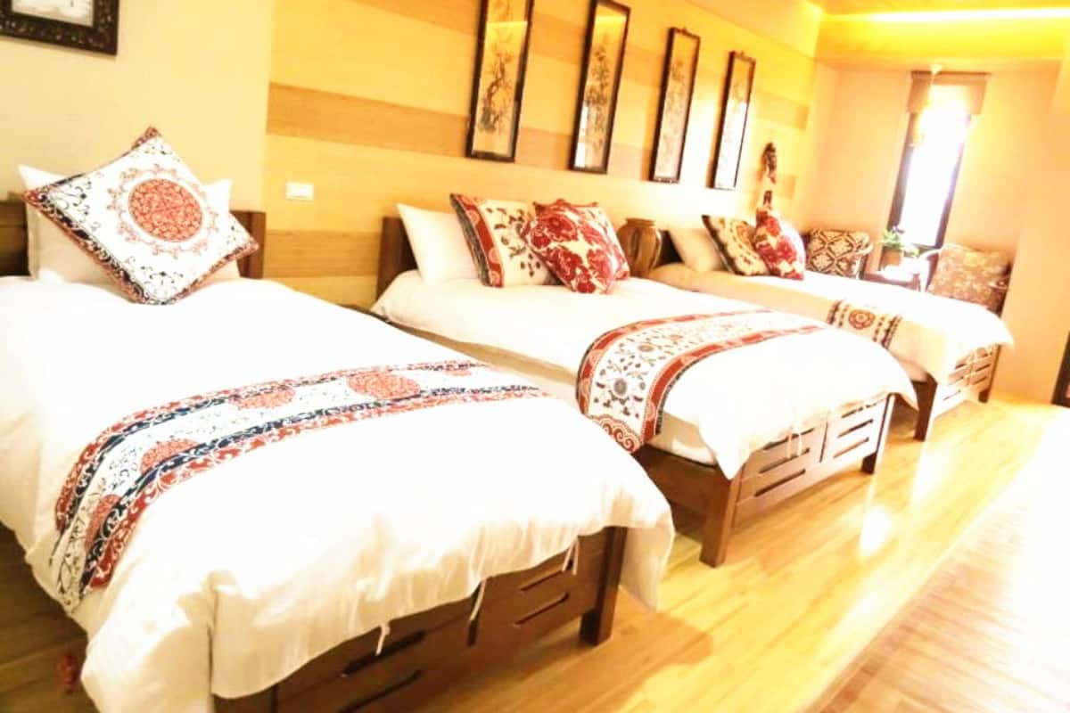 Une chambre d’hôtel avec trois lits, chacun agrémenté de draps et d’oreillers à motifs. La chambre est dotée d’un plancher en bois et présente une palette de couleurs chaleureuses.