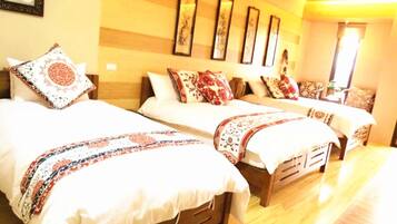 Habitación de hotel con tres camas, cada una con ropa de cama y almohadas estampadas. El piso es de madera y la decoración tiene una paleta de colores cálidos.