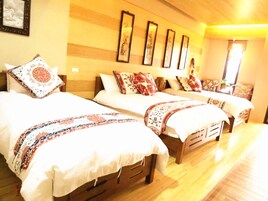Habitación de hotel con tres camas, cada una con ropa de cama y almohadas estampadas. El piso es de madera y la decoración tiene una paleta de colores cálidos.
