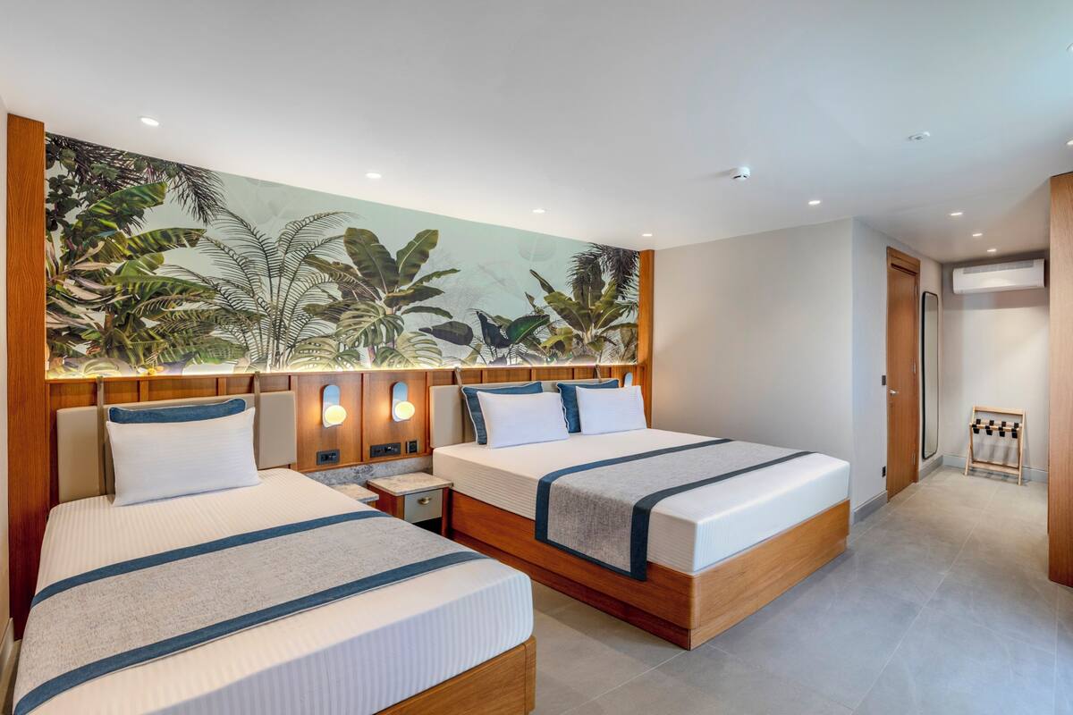 Quarto de hotel com duas camas, um grande mural tropical e um pequeno espaço de estar.