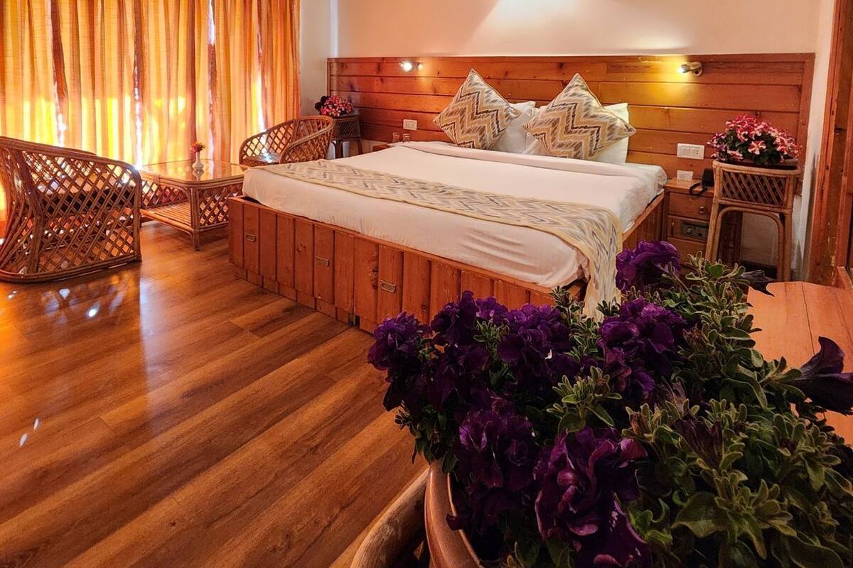 A bedroom with a wooden ceiling, a bed with patterned bedding, a nightstand, and a wicker chair.