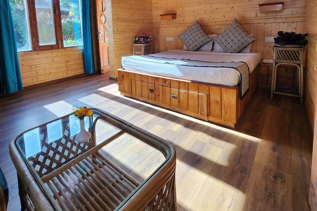A wooden cabin interior with a bed, a glass table, and a chair.