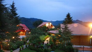 Un resort con varias construcciones, un jardín cuidado y montañas al fondo.