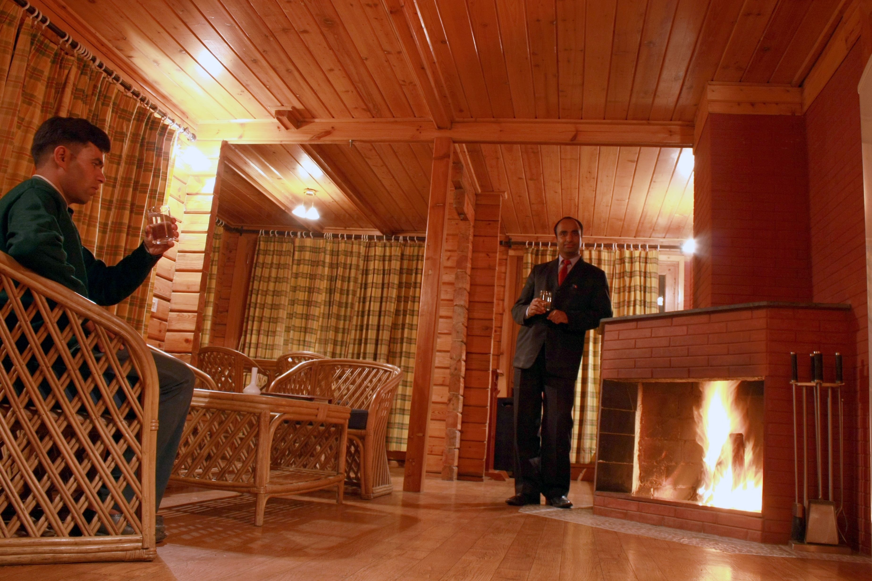 A wooden interior with a fireplace, wicker furniture, and a person holding a glass.