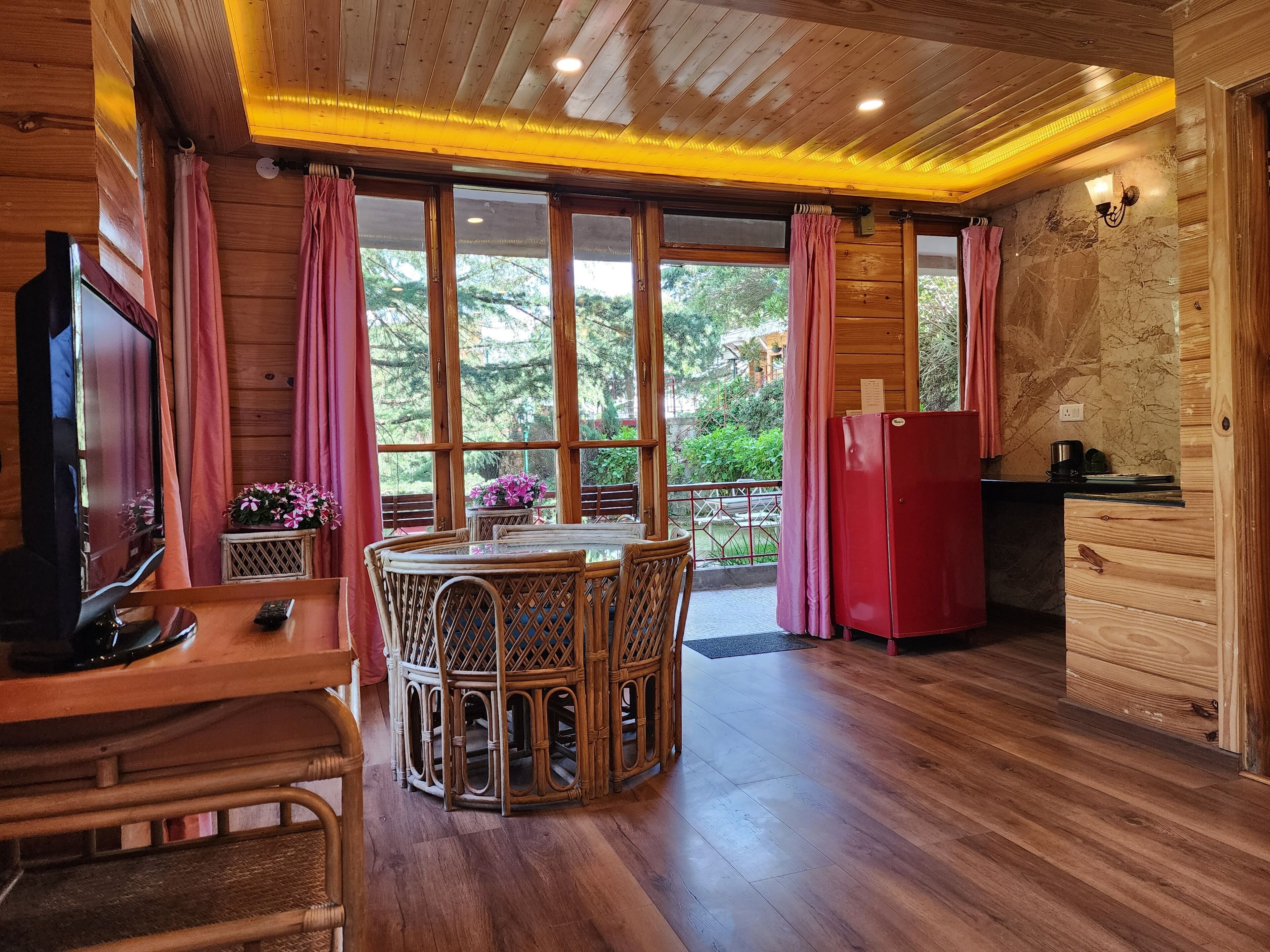 A wooden cabin interior with a dining area, kitchen, and large windows.