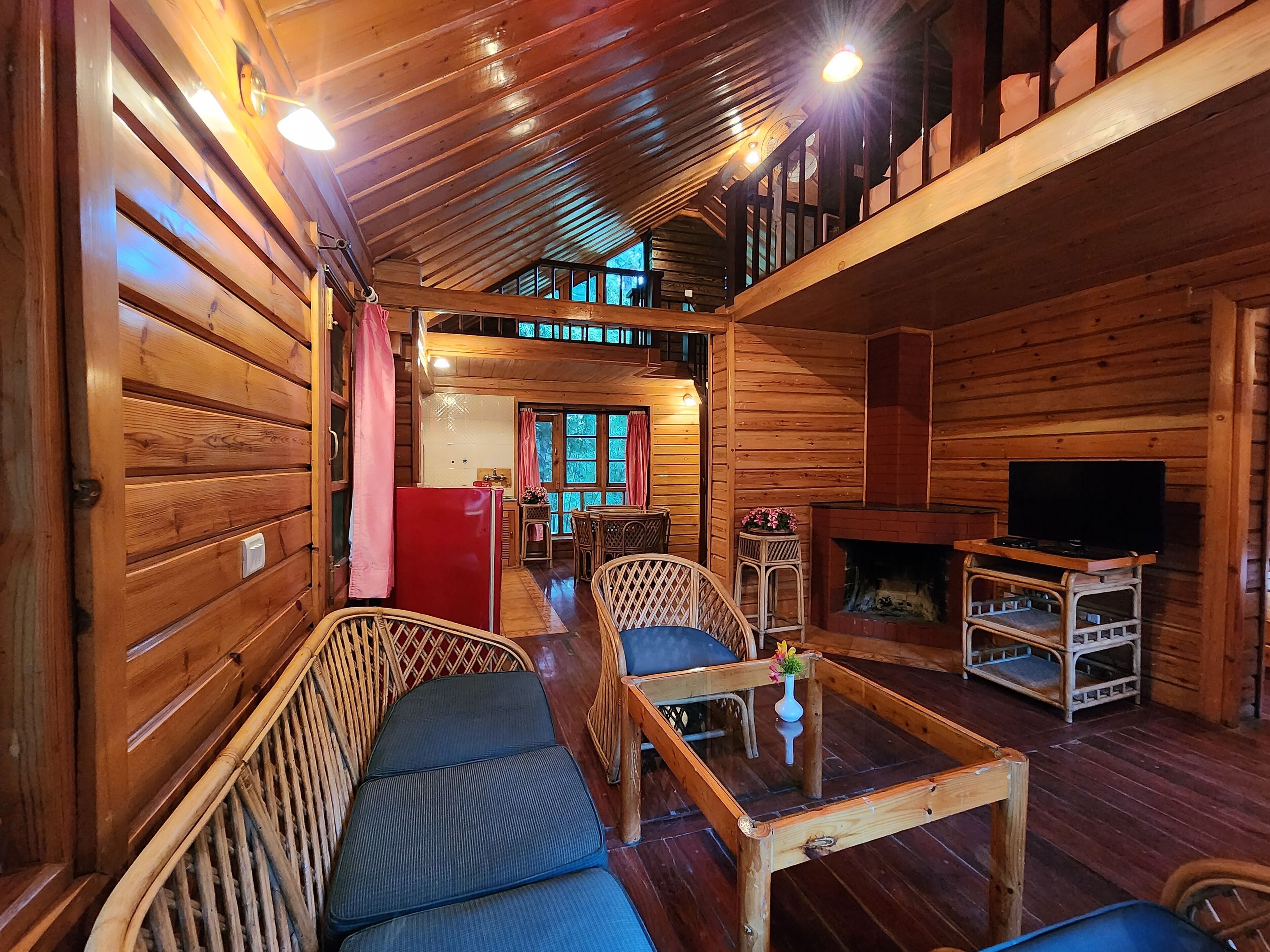 L’intérieur d’un chalet confortable en rondins de bois comprend un coin repas, des sièges avec des coussins, une cheminée et un téléviseur.