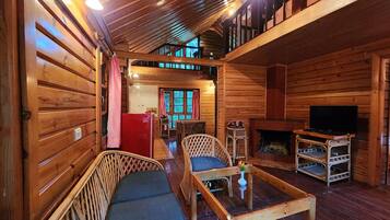 L’intérieur d’un chalet confortable en rondins de bois comprend un coin repas, des sièges avec des coussins, une cheminée et un téléviseur.