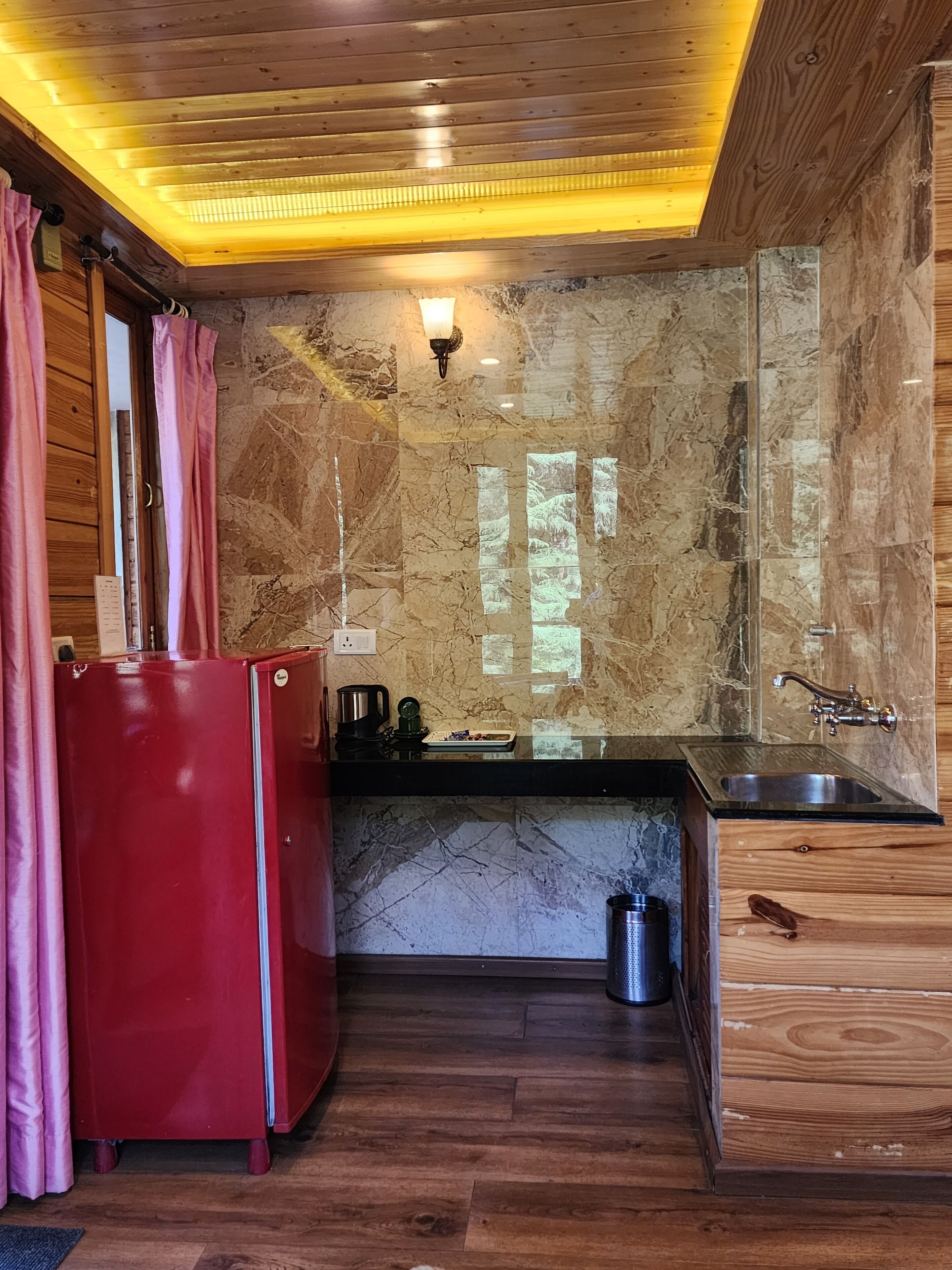 A kitchen with a red refrigerator, wooden cabinets, a marble backsplash, and a wooden ceiling with recessed lighting.