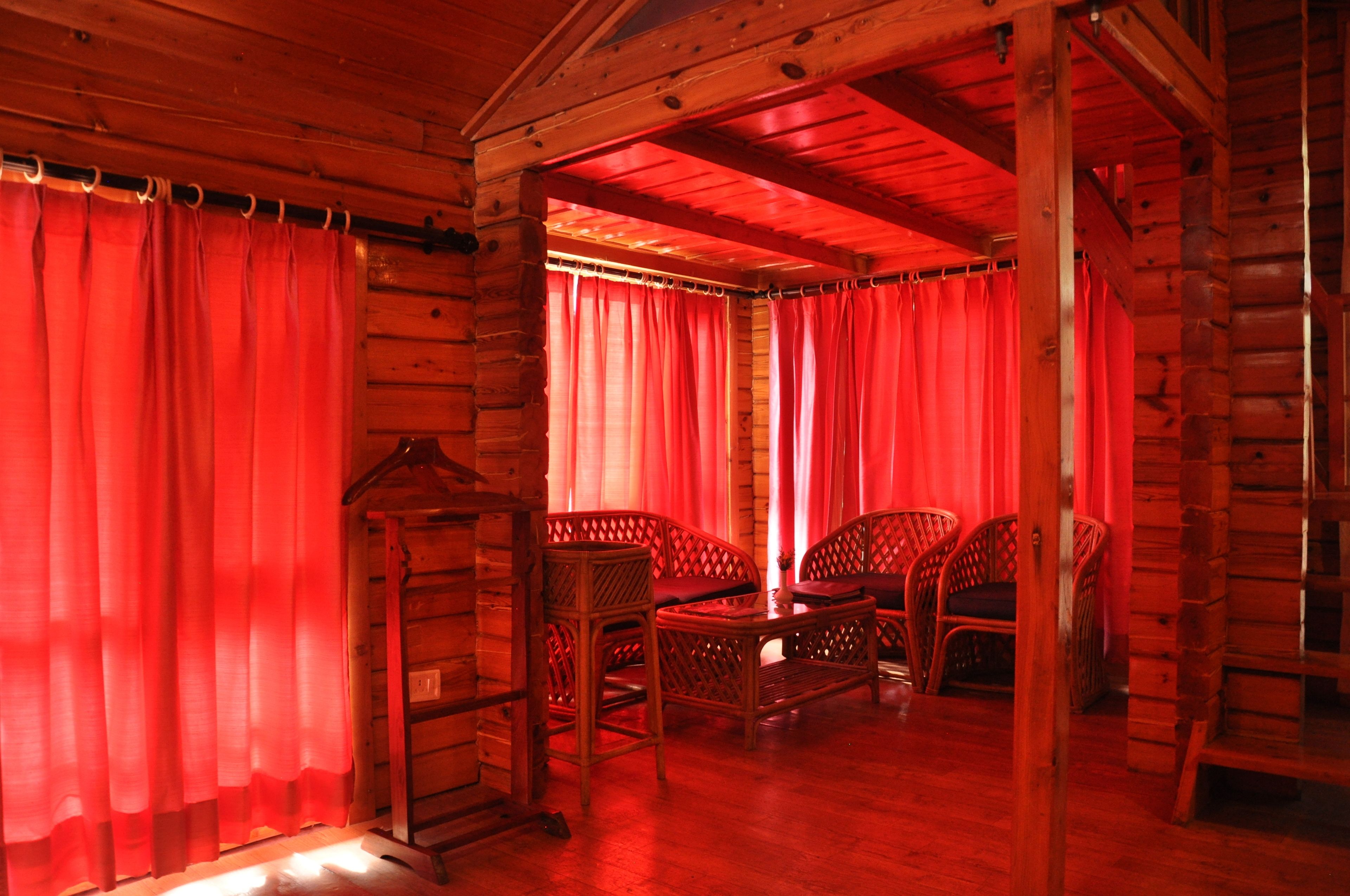 A log cabin interior with red curtains, wicker furniture, and a wooden ceiling.