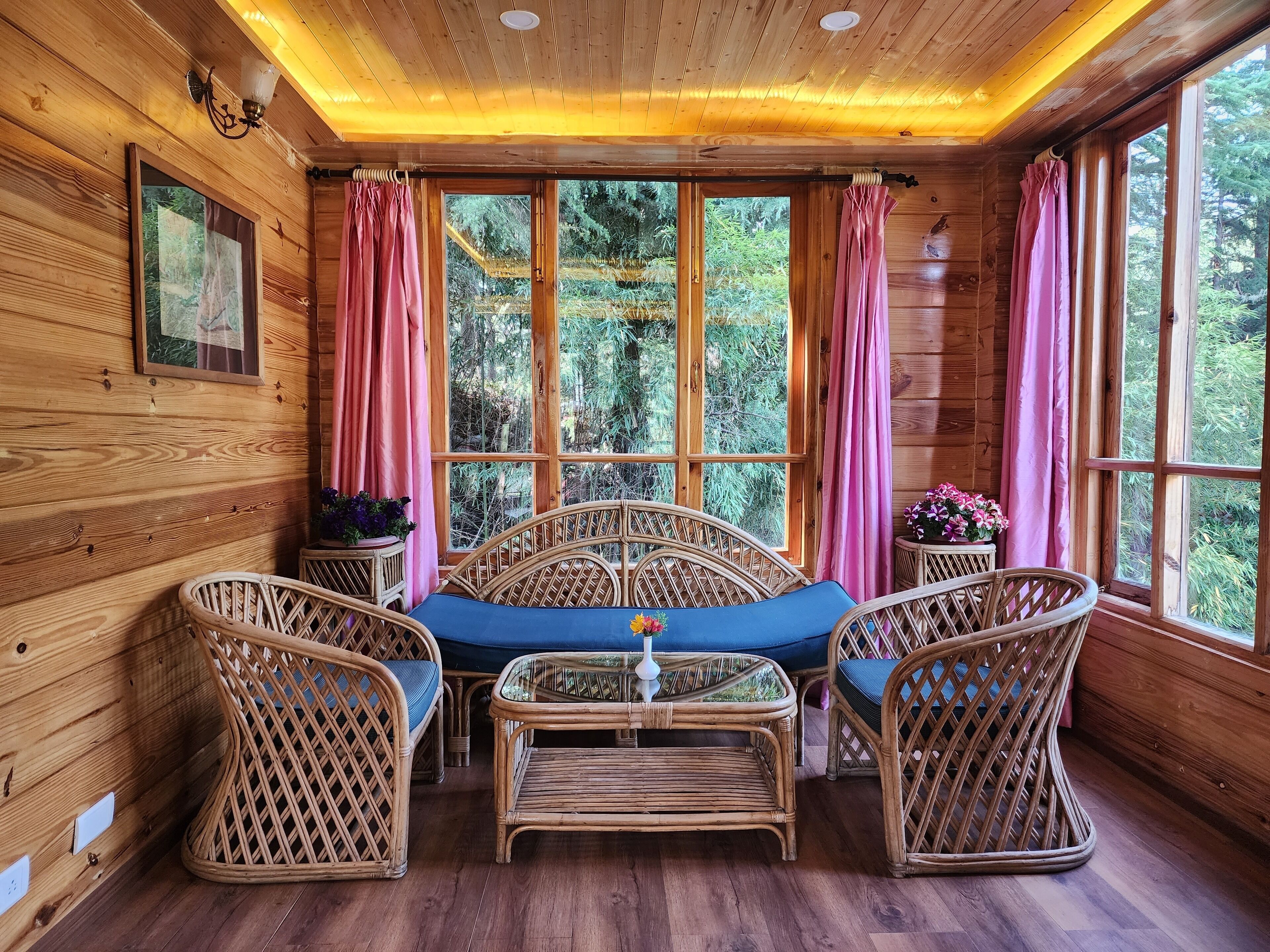 Una cabaña acogedora de madera con un ventanal grande, muebles de mimbre y un cuadro en la pared.