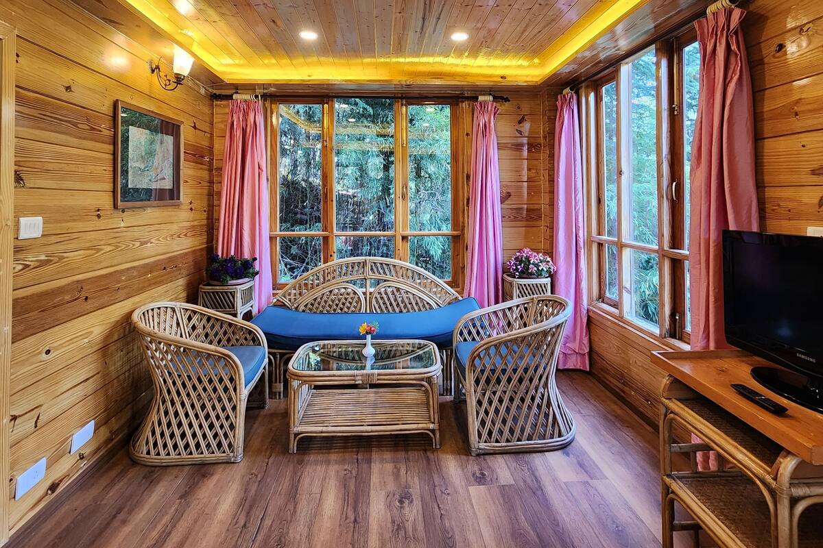 A cozy cabin interior with wooden walls, a central seating area with a table, and large windows with curtains.