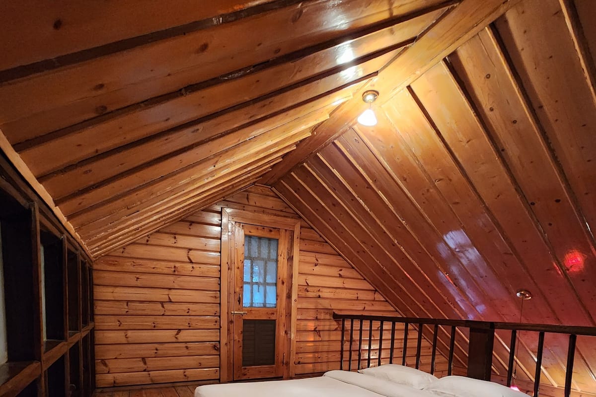 A wooden attic bedroom with a bed, wooden walls, a window, and a railing.