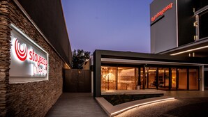 A modern hotel exterior with a stone facade, a large illuminated sign, and a well-lit entrance. - StayEasy Maputo (Maputo)