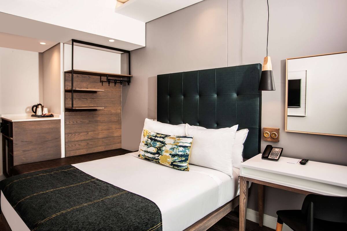 Moderni hotellihuone, jossa on suuri sänky, työpöytä ja vaatekaappi.