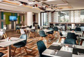 A modern dining area with multiple tables and chairs, a flat-screen TV, and large windows offering a view.
