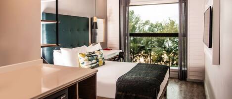 Habitación de hotel moderna con una cama grande, un escritorio y una ventana que da a vistas de árboles.