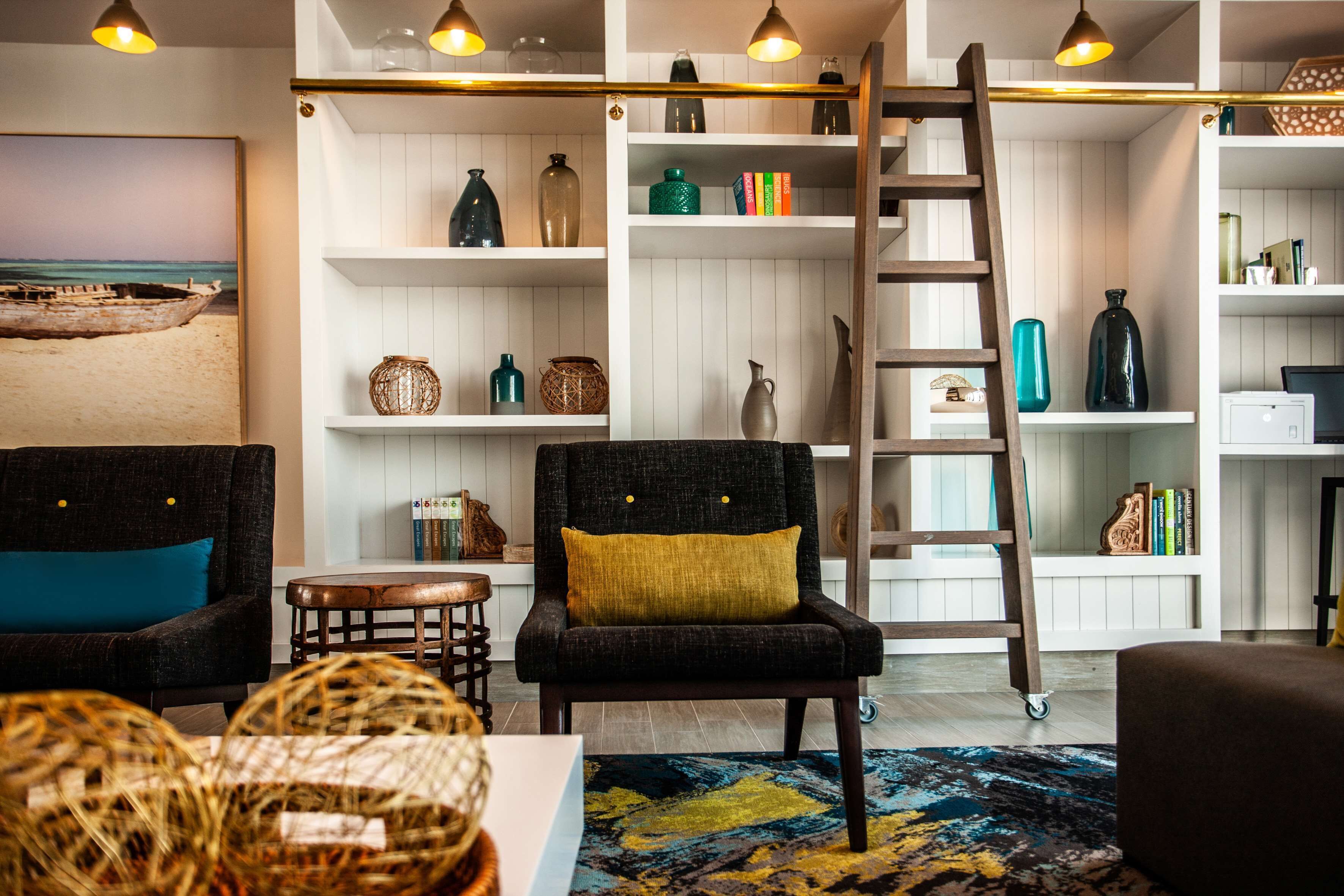 A modern living room with a black armchair, a wooden ladder, and shelves with decorative items.
