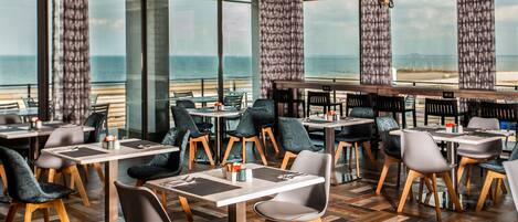A restaurant with a view of the ocean, featuring modern furniture and large windows.