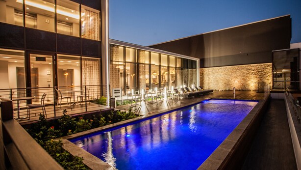 A modern hotel with a swimming pool, outdoor seating, and a well-lit interior. - StayEasy Maputo (Maputo)
