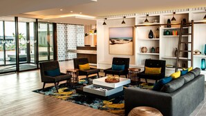 A modern living room with a sofa, armchairs, and a coffee table. There are bookshelves with decorative items and a painting of a beach scene. - StayEasy Maputo (Maputo)