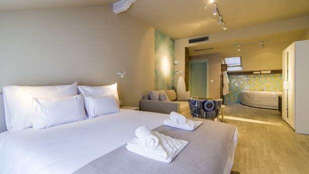 Una habitación de hotel con una cama grande, un sofá, una mesita y un baño con bañera.
