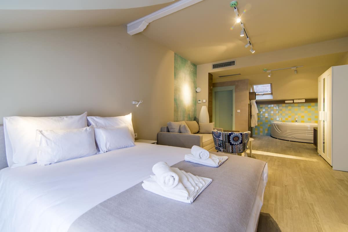 A hotel room with a large bed, a sofa, a small table, and a bathroom with a bathtub.