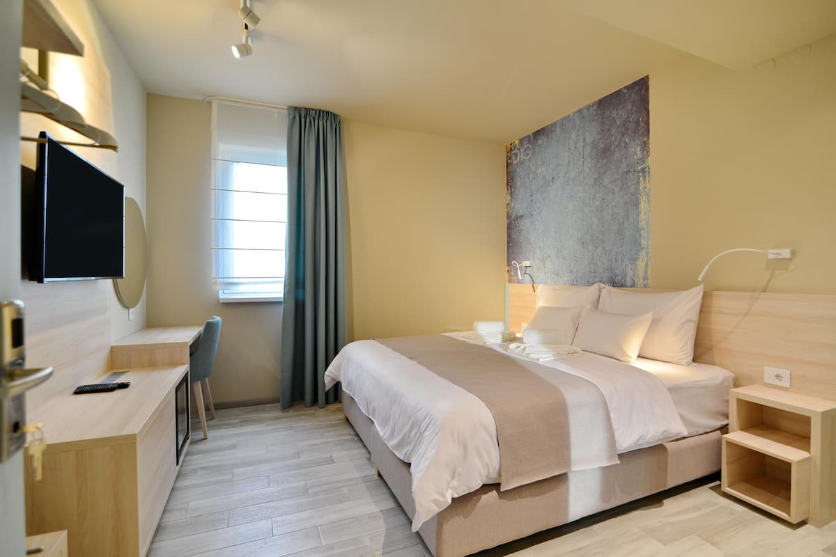 A modern hotel room with a bed, desk, chair, and a large abstract painting on the wall.