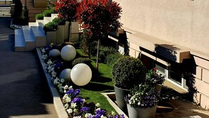 Un edificio moderno con fachada color beige, grandes ventanales y un jardín bien cuidado con diversas plantas y flores.