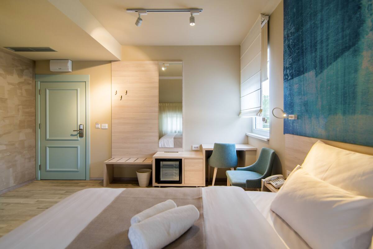 A hotel room with a bed, a desk, a chair, a phone, and a window.