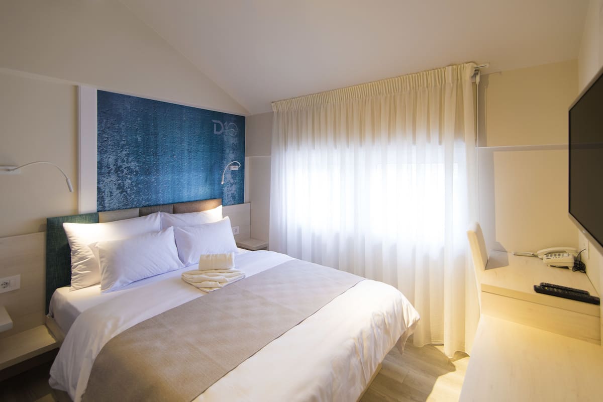 A hotel room with a bed, a desk with a phone and remote, a TV, and a window with curtains.