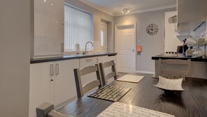 Een moderne keuken met witte kastjes, een zwarte aanrechtblad en een eethoek met een houten tafel en stoelen.