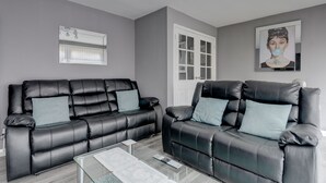 Een moderne woonkamer met twee zwarte leren banken, een glazen salontafel en een witte deur met ruitpanelen.