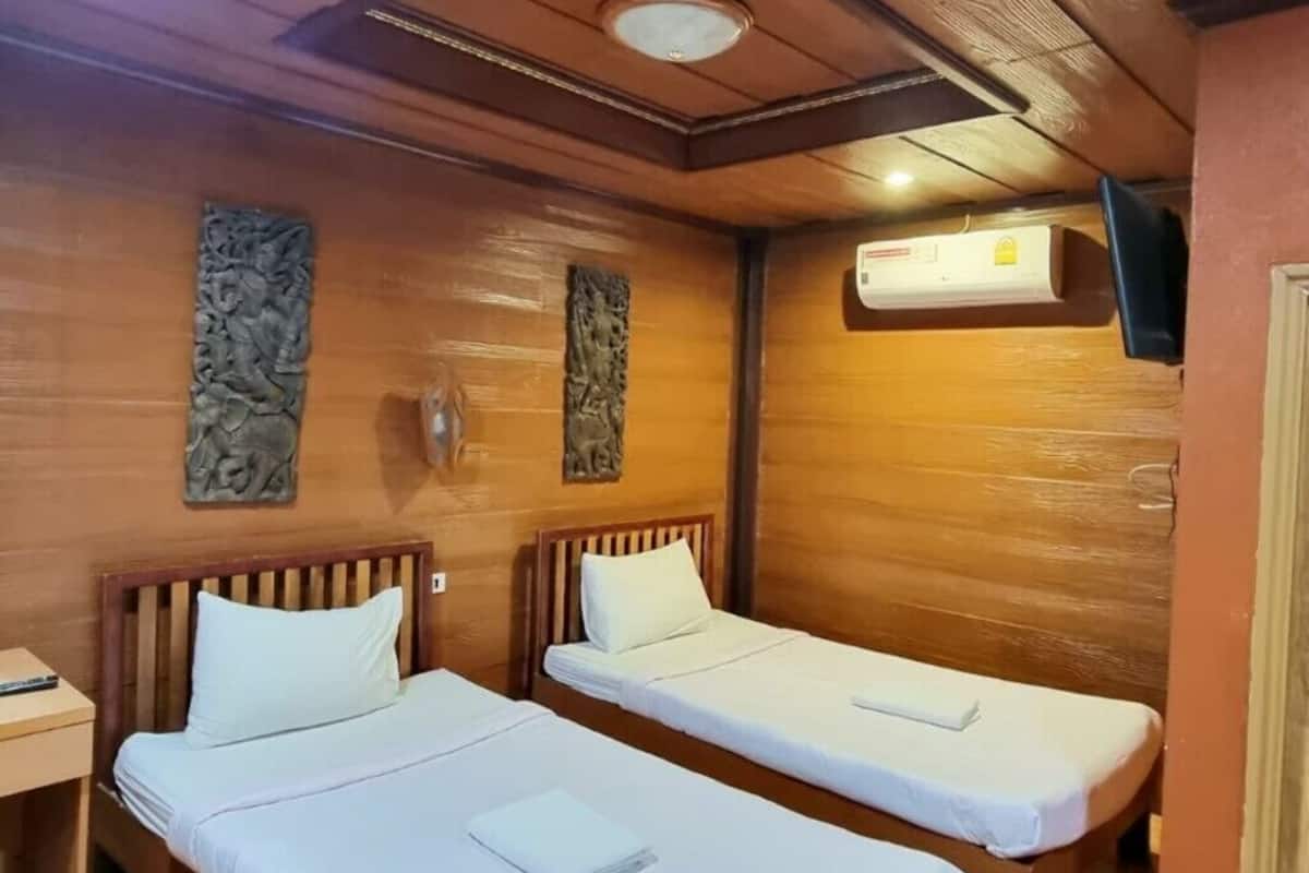 A room with two wooden beds, a ceiling light, and an air conditioning unit.