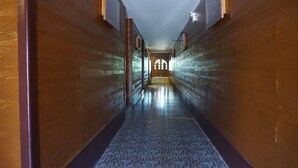 A long, narrow hallway with wooden walls and a patterned floor, leading to a bright, arched doorway at the end. - Lampang Bouteak Resort (Lampang)