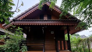 A traditional wooden house with a tiled porch, steps leading to the entrance, and a garden area with potted plants. - Lampang Bouteak Resort (Lampang)