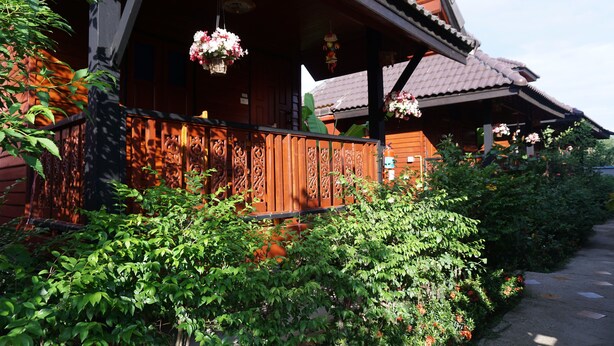 A traditional wooden building with a balcony, surrounded by lush greenery and hanging flower baskets. - Lampang Bouteak Resort (Lampang)