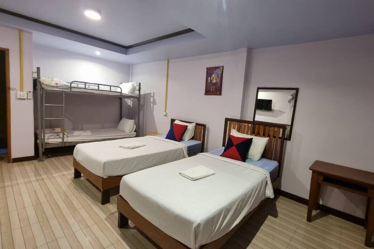 A hotel room with two beds, a bunk bed, a small wooden table, and a mirror on the wall.