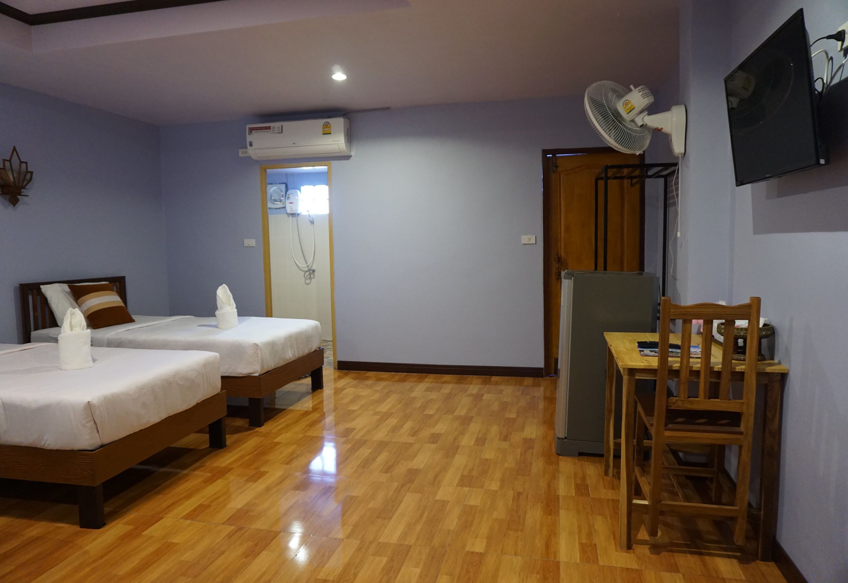 Una habitación con dos camas, piso de madera, un escritorio con silla, un refrigerador y un equipo de aire acondicionado.