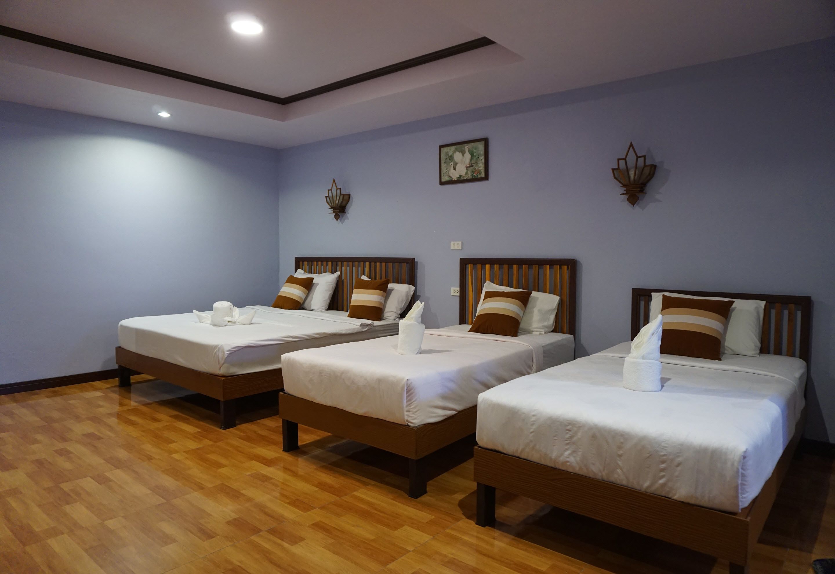 Une chambre d’hôtel avec trois lits simples, des têtes de lit en bois et un plancher en bois.