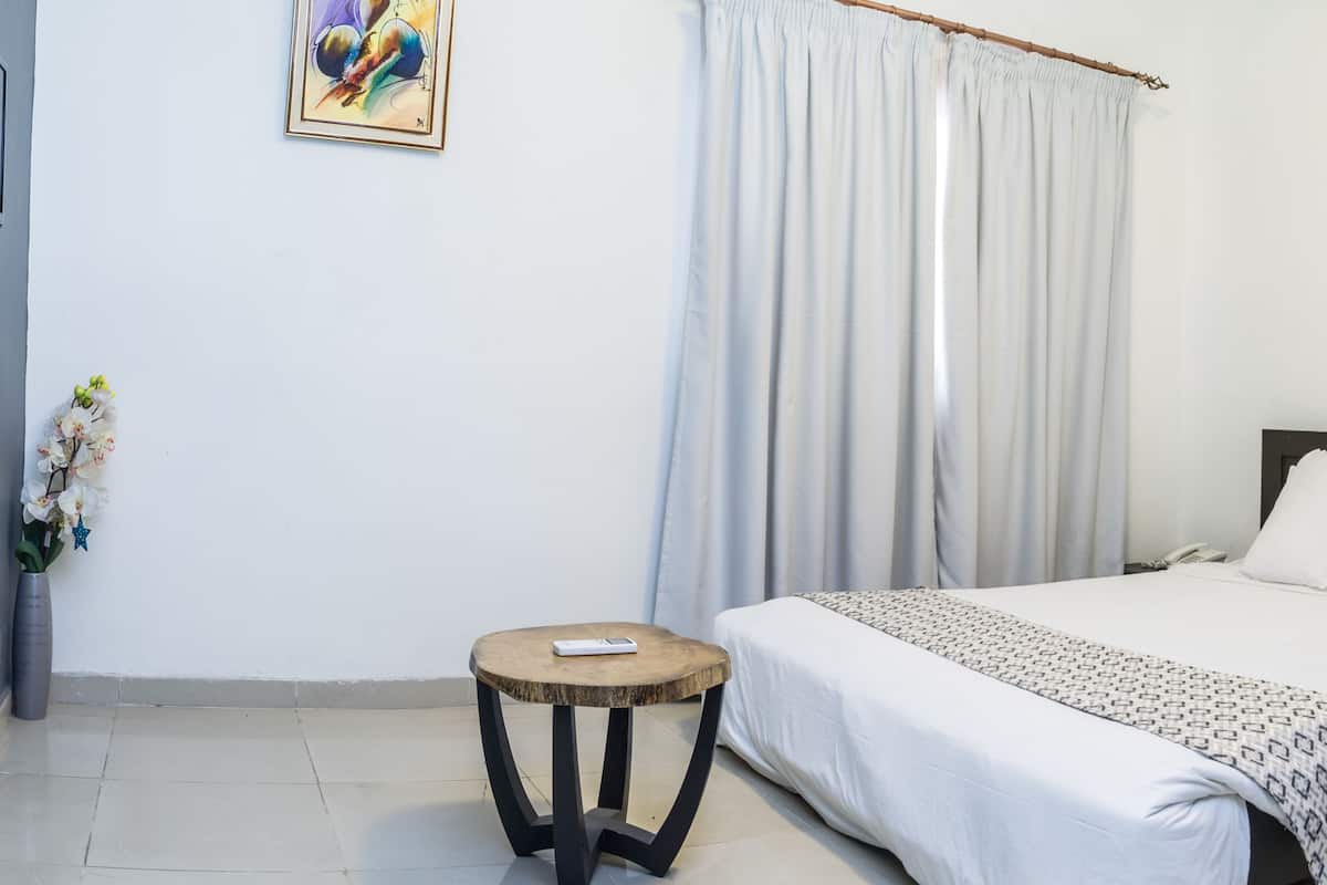 A hotel room with a bed, bedside table, and a small round table with a remote control.