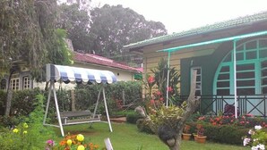 A garden with a swing set, a gazebo, and a house with a green roof and a blue window frame.
