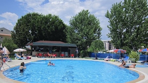 A swimming pool with lounge chairs and umbrellas, surrounded by trees and a building with a red roof.