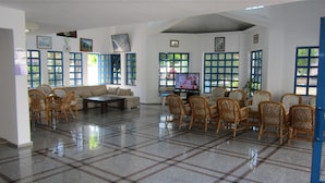 A spacious living area with a tiled floor, a sofa, and several wicker chairs.