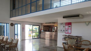 A spacious lobby with a checkered floor, wicker furniture, and a reception area with a counter and informational posters.